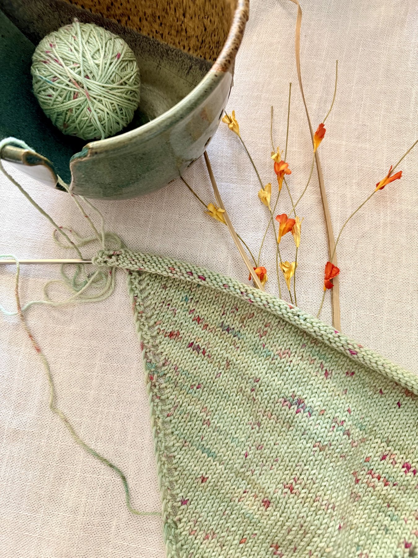 Sweetbriar Bandana in progress with yarn skeins and pottery bowl